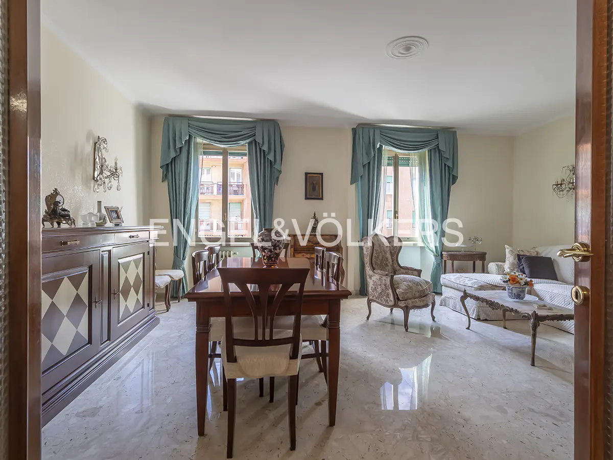 A bright living room with a dining table, chairs, a sofa, and two windows with blue curtains.