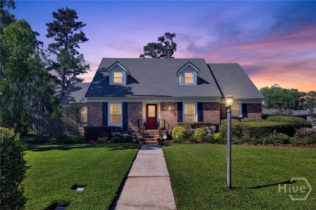 Two-story brick house with a red door, black shutters, and a gray roof at dusk. A sidewalk leads to the front door.