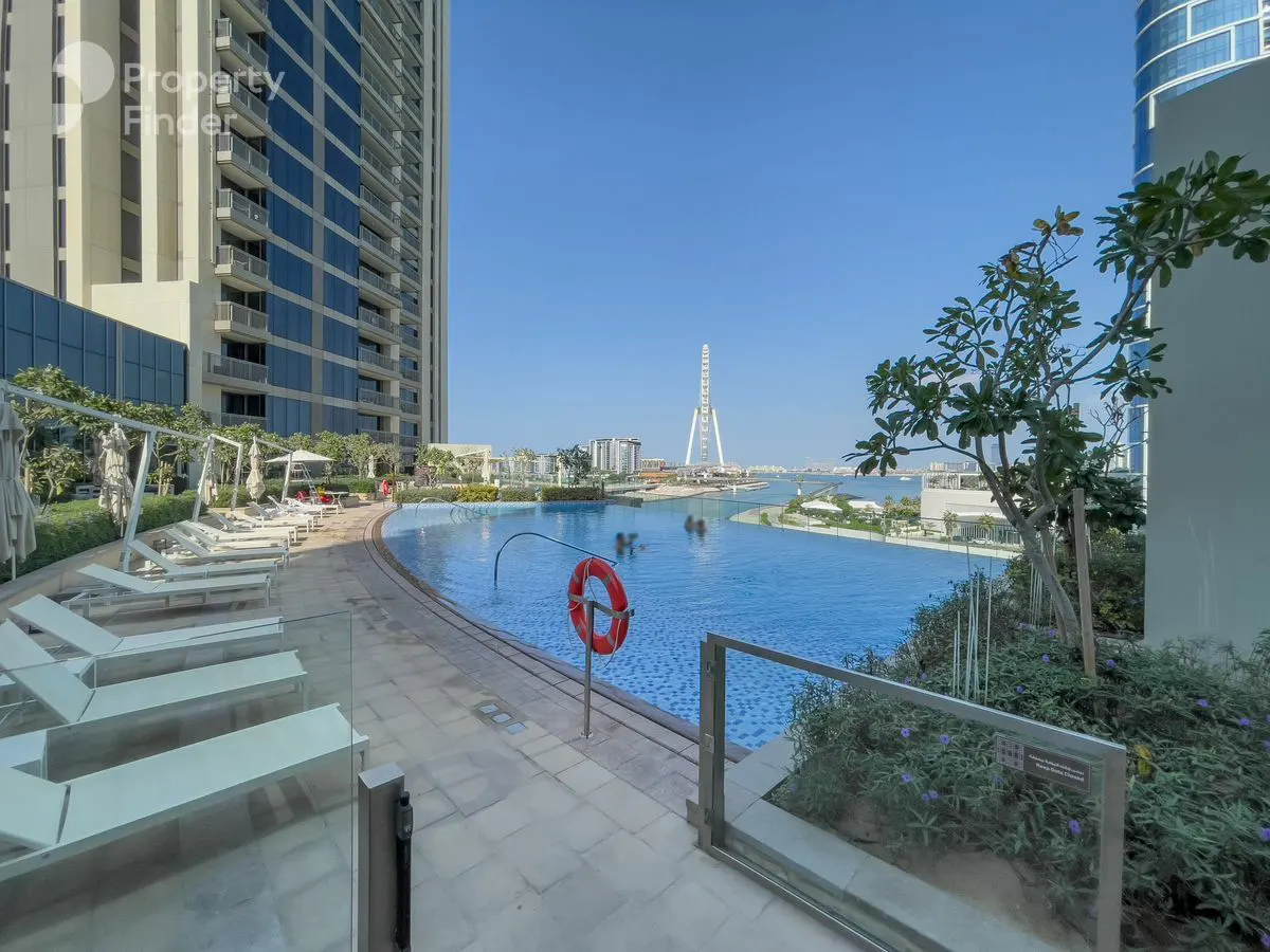 A wide shot of a blue pool with lounge chairs, a life preserver, and a view of the Ain Dubai Ferris wheel in the background.