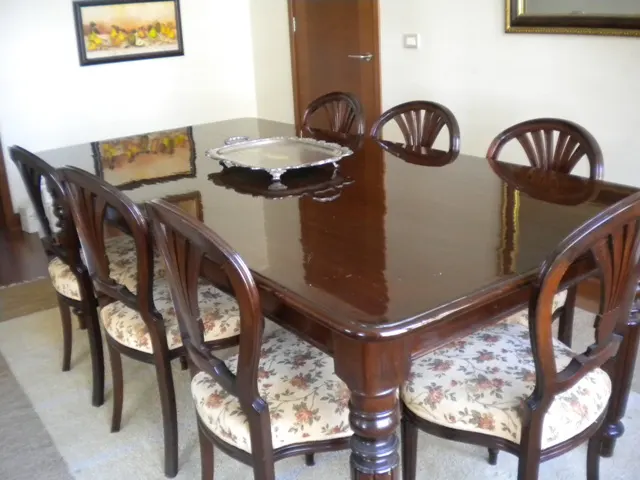 A dining room features a dark wood table with six chairs with floral patterned cushions and a silver tray on top.