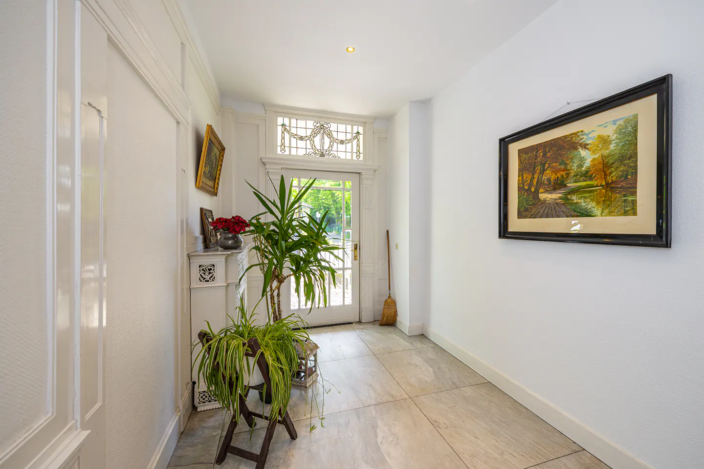 Bright entryway with white walls, tiled floor, a potted plant, and a landscape painting hanging on the wall.
