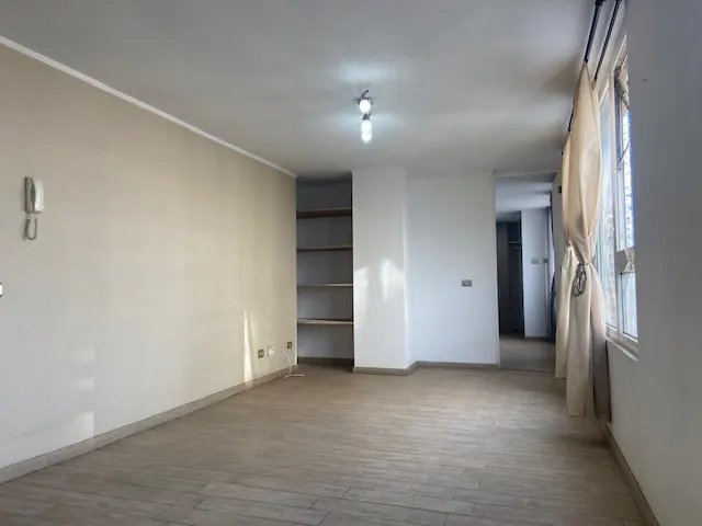 Empty room with light-colored walls, wood-look tile flooring, built-in shelves, and a window with beige curtains.