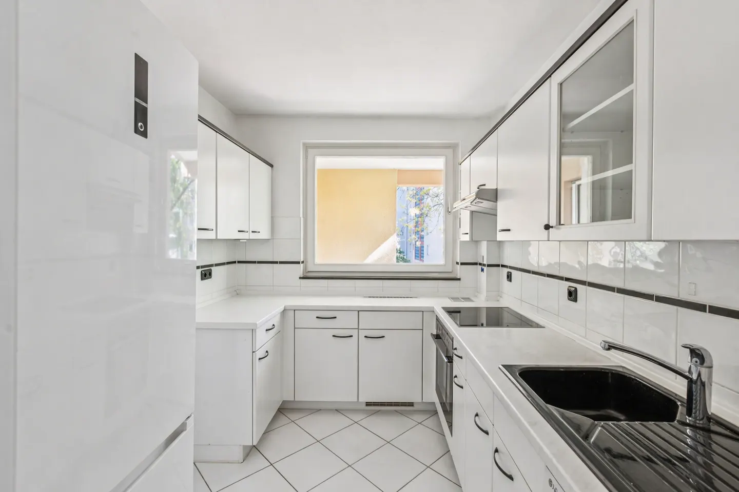 Bright kitchen with white cabinets, black hardware, and a black sink. A window provides natural light. The floor is tiled in a diamond pattern.