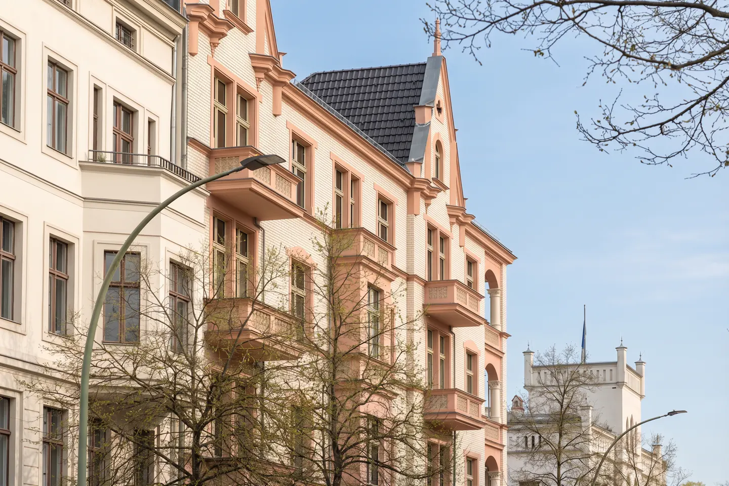 Exterior view of multi-story buildings with balconies, white and pink trim, and a blue sky background.