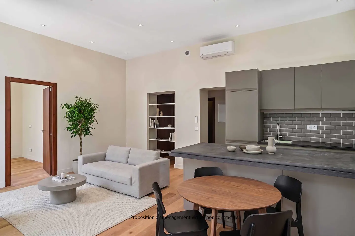 Open-concept living space with a gray sofa, round coffee table, and a wood dining table with black chairs near a gray kitchen.