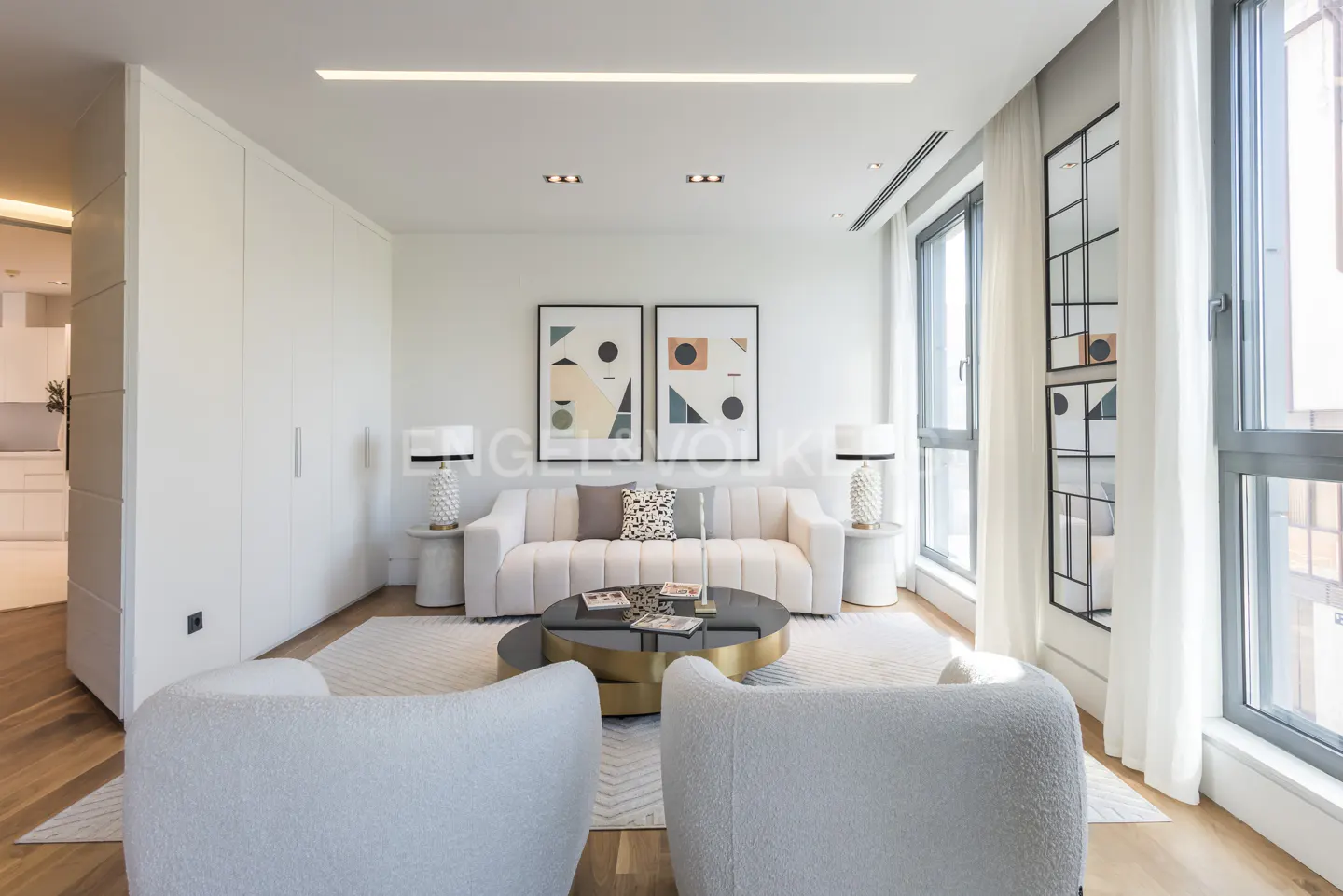 Bright living room with white sofa, chairs, and rug. Two abstract art pieces hang above the sofa. A round coffee table sits in the center.
