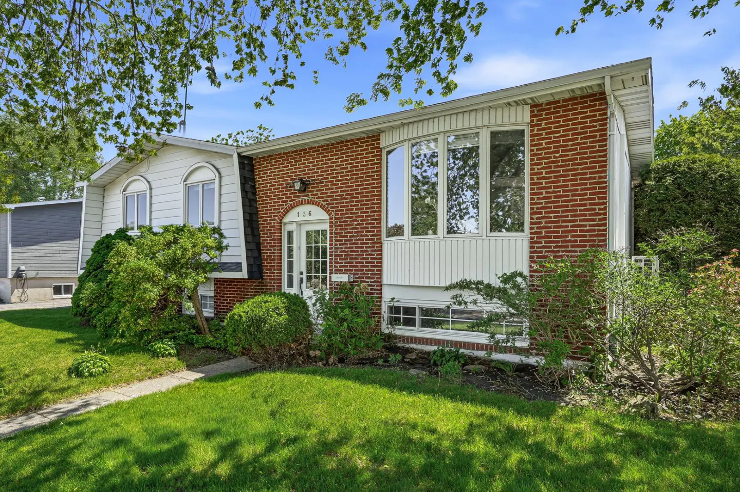 Two-story house with brick and white siding, green lawn, and trees under a blue sky.