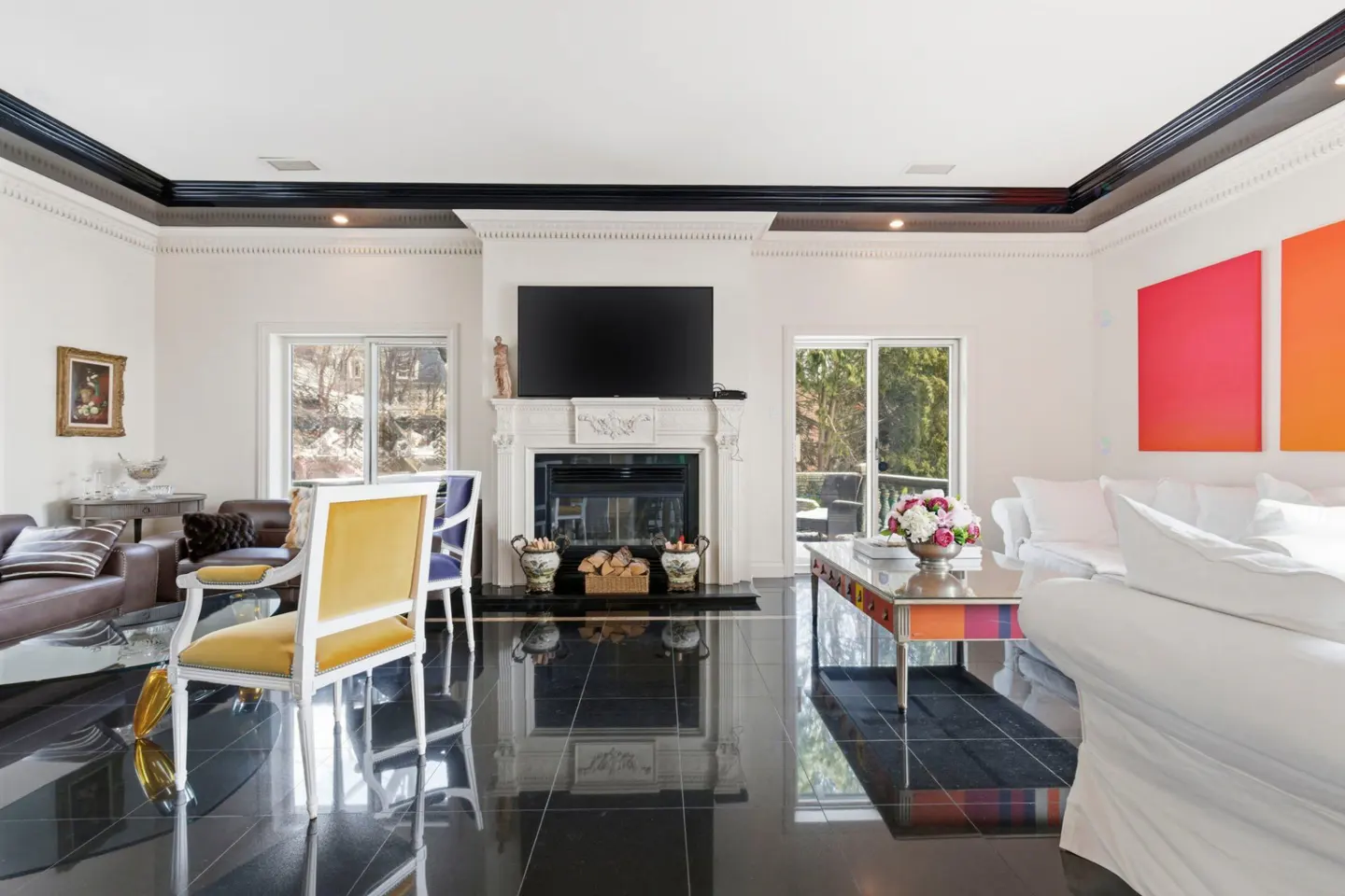 A bright living room with black tile floors, a white fireplace with a TV above, and colorful artwork.