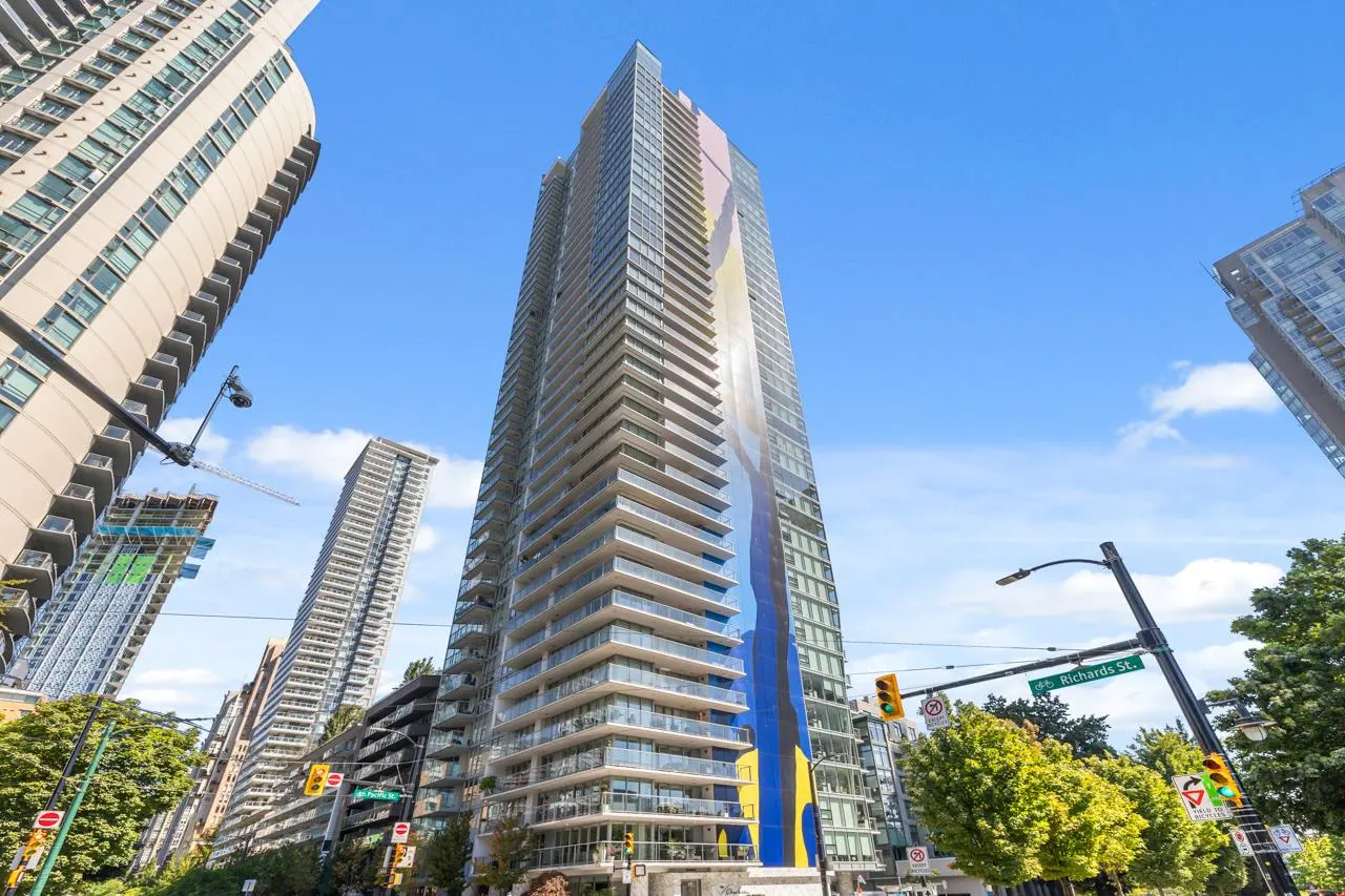 View of a tall, modern condo building with blue and yellow art on its side, set against a clear blue sky.