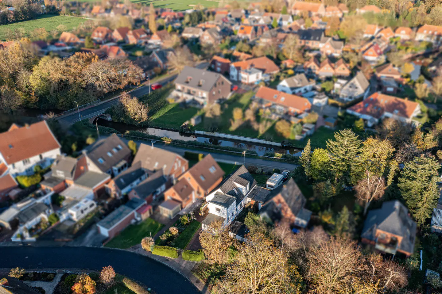 Aerial view of a quaint village with houses, trees, and a small river running through it. The houses have red and gray roofs.