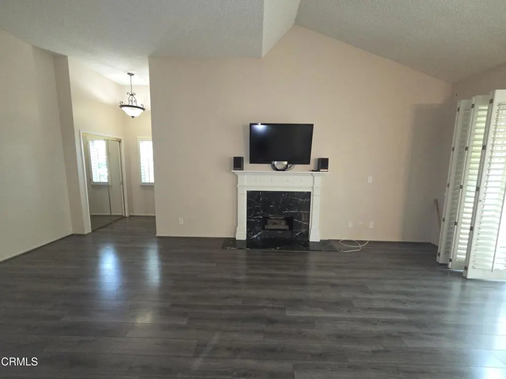 Living room with dark wood floors, a black marble fireplace with a TV, and white shutter doors.