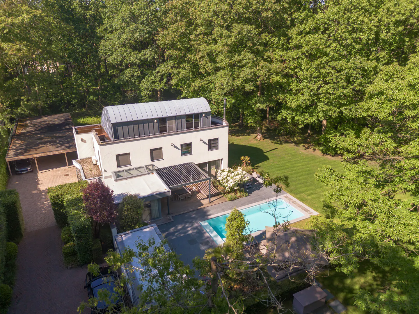 Aerial view of a modern white house with a pool, patio, and lush green trees.