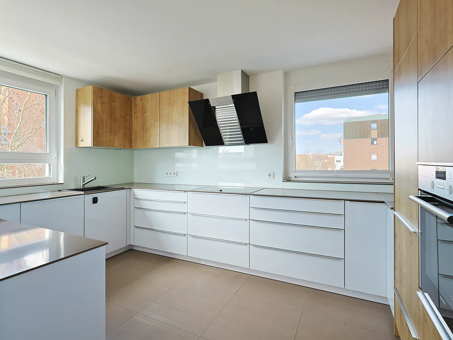 Bright kitchen with white cabinets, light wood accents, and stainless steel appliances. A black range hood is centered above the counter.