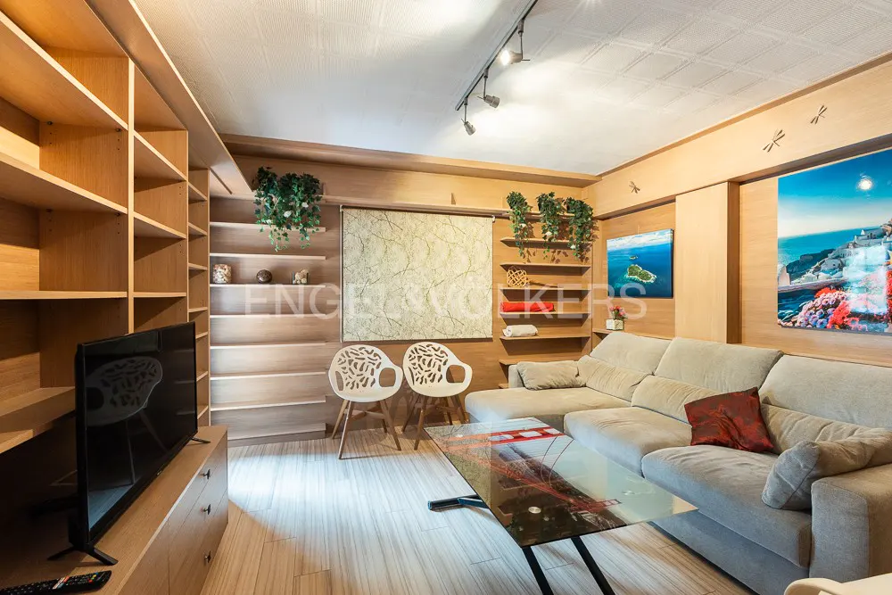 Living room with light wood paneling, built-in shelves, and a beige sectional sofa. A glass coffee table sits in front of the sofa.