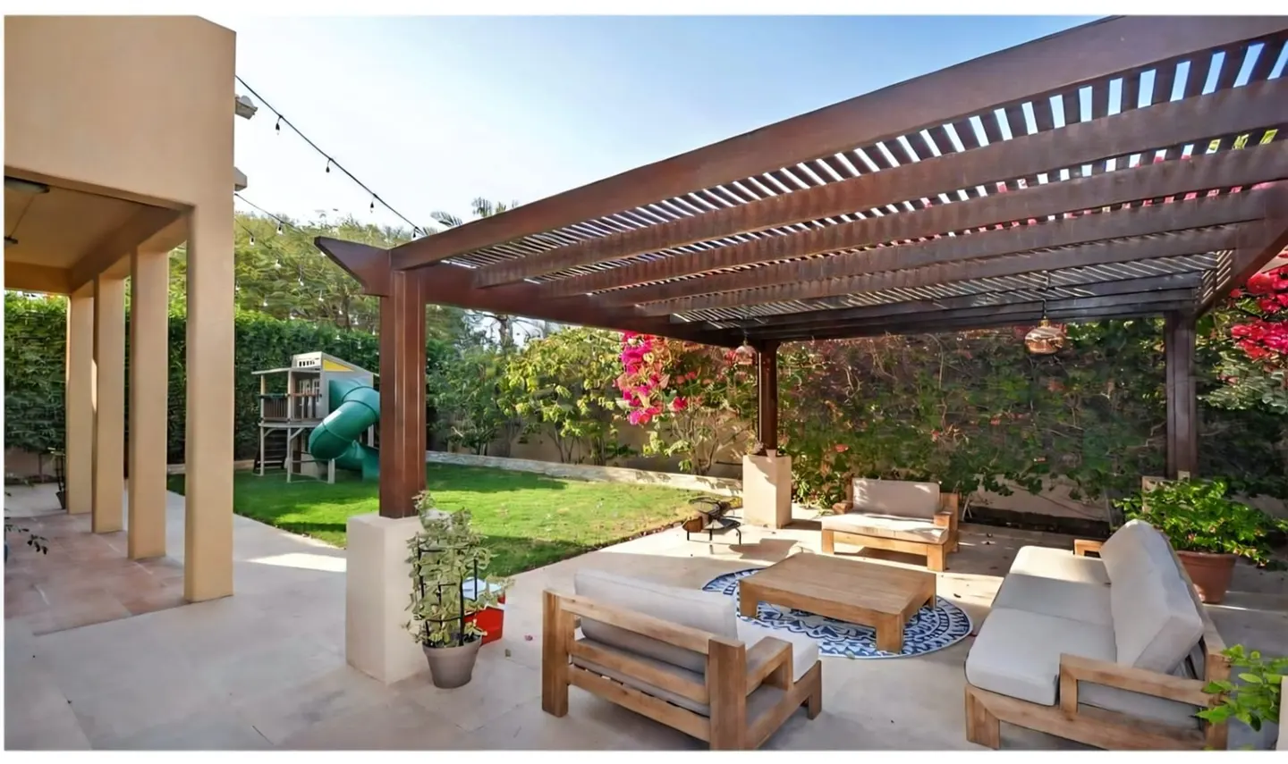 Outdoor patio with a wooden pergola, comfortable seating, a coffee table, and a backyard with a children's play set.