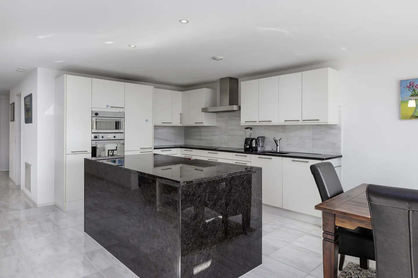 Modern kitchen with white cabinets, black granite island, stainless steel appliances, and marble floors.