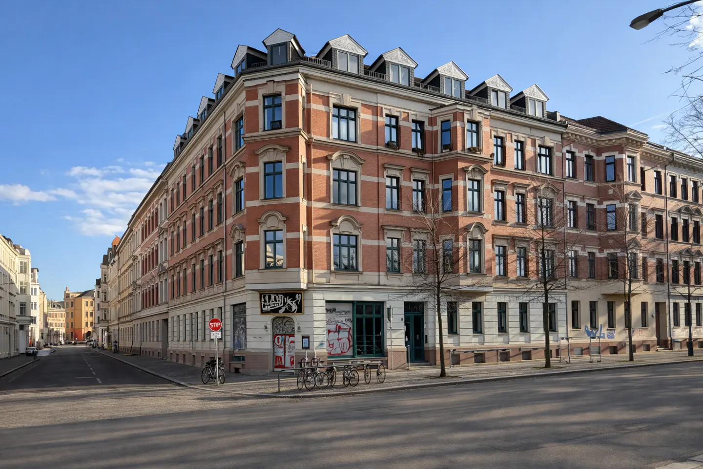 Street view of a long, red brick apartment building with many windows under a blue sky.