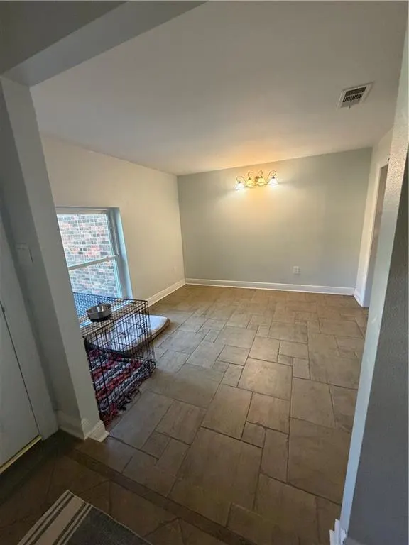 A bright, empty living room with tan tile flooring and light green walls. A dog crate sits near a window.