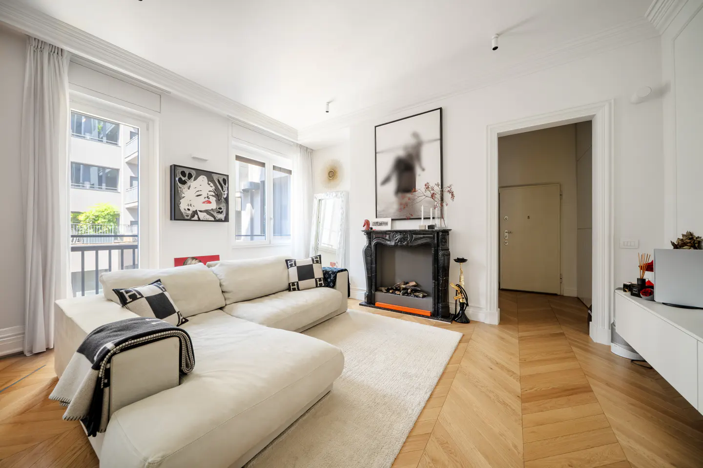 Bright living room with white walls, herringbone wood floors, and a large white sectional sofa. A black fireplace and art add contrast.