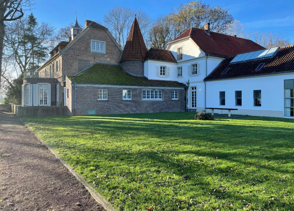 Exterior view of a multi-sectioned building with brick and white siding, red tile and mossy roofs, and a large green lawn.