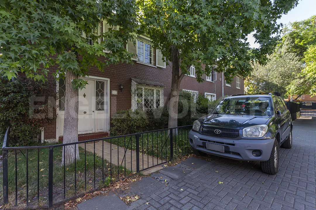 A two-story brick townhouse with a white door and a dark green SUV parked in front.