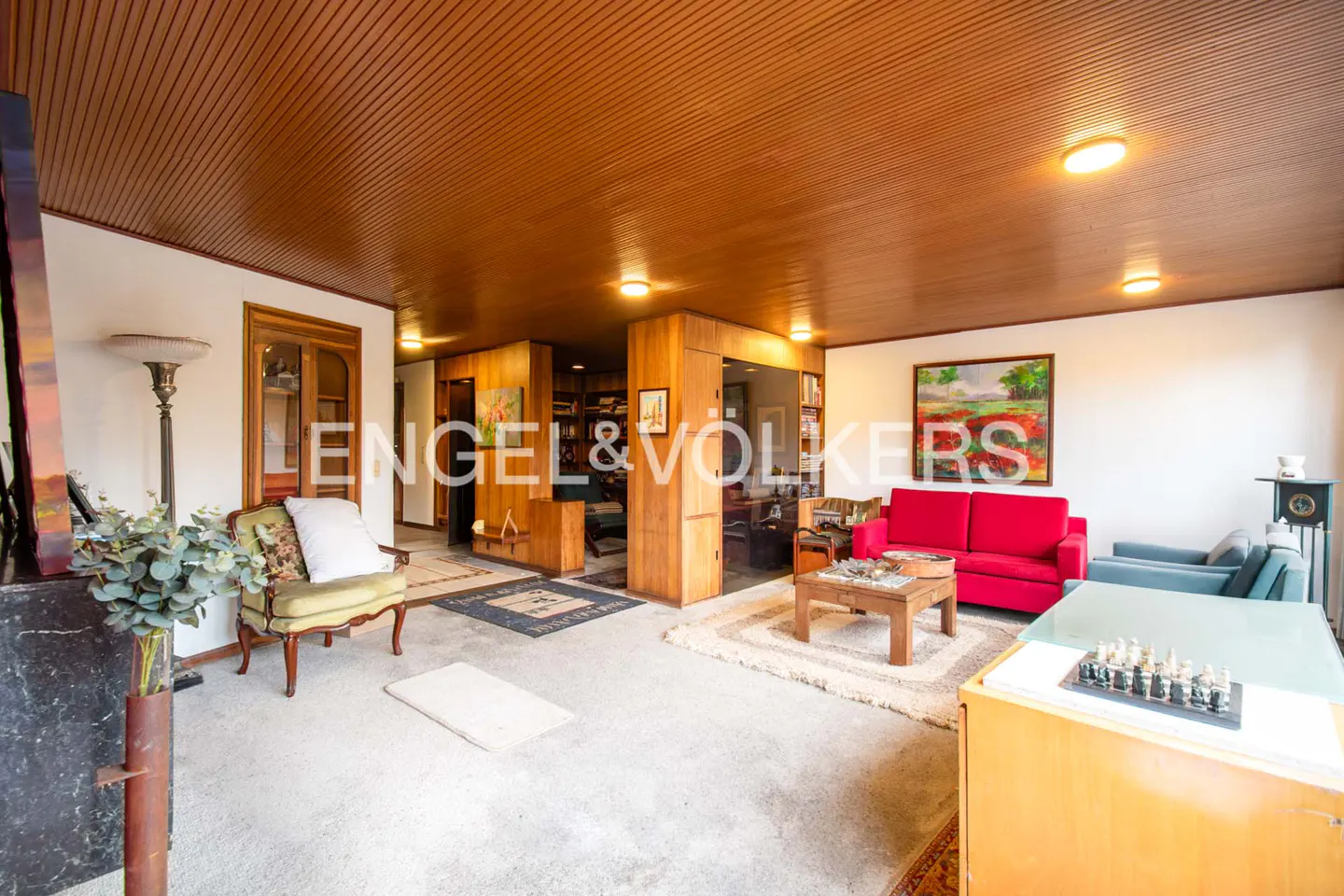 Living room with wood-paneled ceiling, red sofa, green armchair, coffee table, and a chess set on a table.