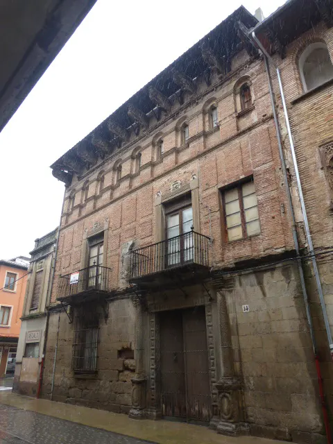 A three-story brick building with balconies and a large wooden door. The building has a stone foundation and decorative elements.