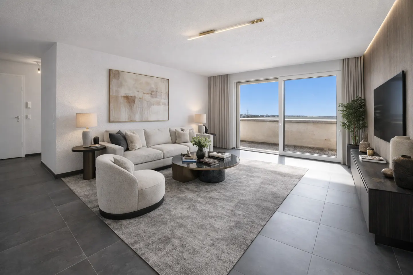 Bright living room with a beige sofa, round coffee table, and a large window leading to a balcony with a blue sky view.