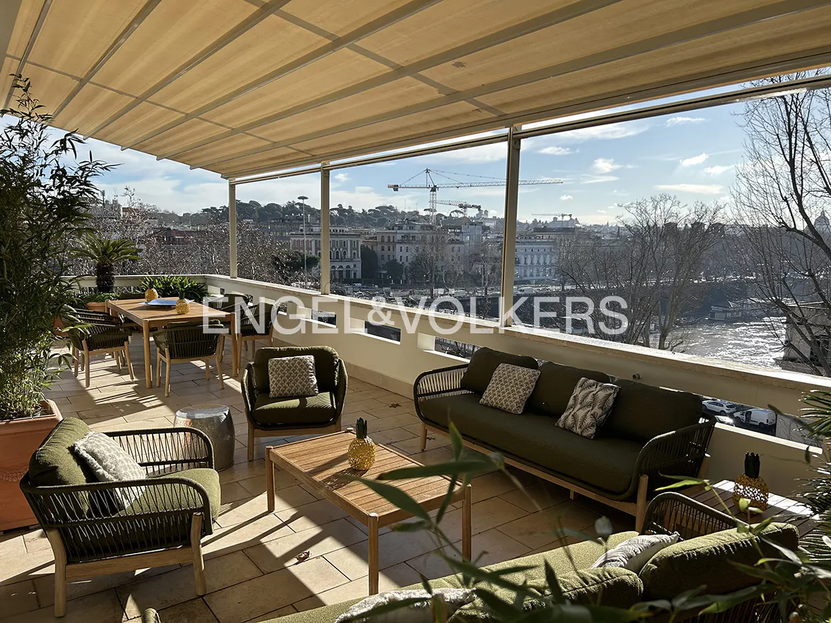 Spacious balcony with olive green outdoor furniture, a dining set, and a panoramic city view under a retractable awning.
