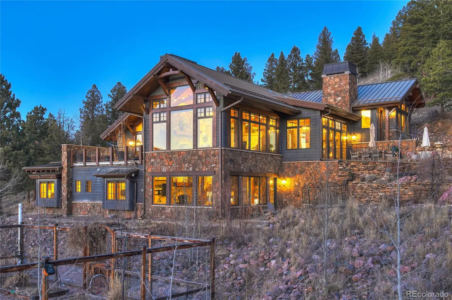 Exterior of a large, multi-story home with stone and wood accents, nestled in a wooded area at dusk.