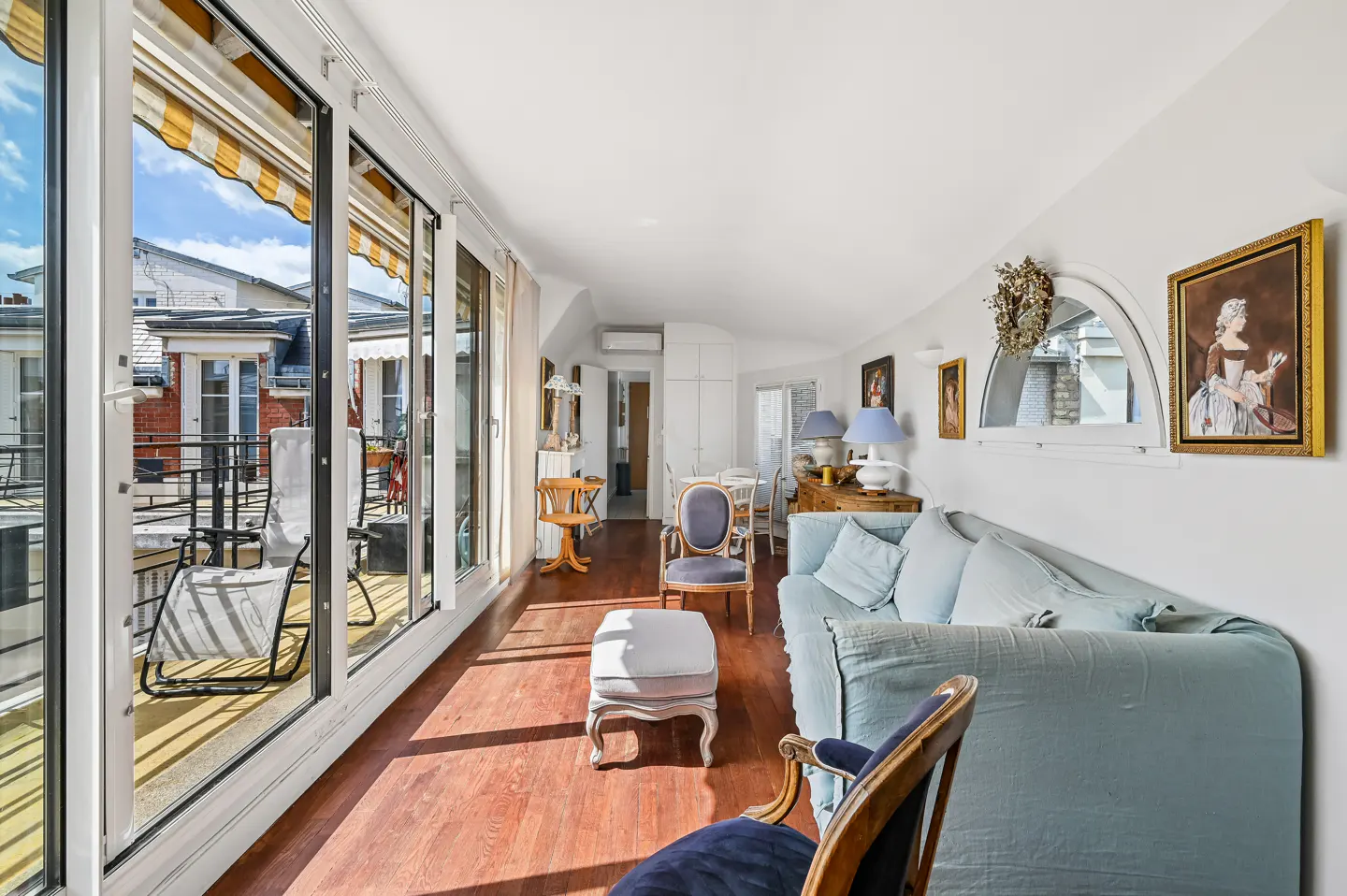 Bright living room with hardwood floors, blue sofa, and balcony with city views through large windows.