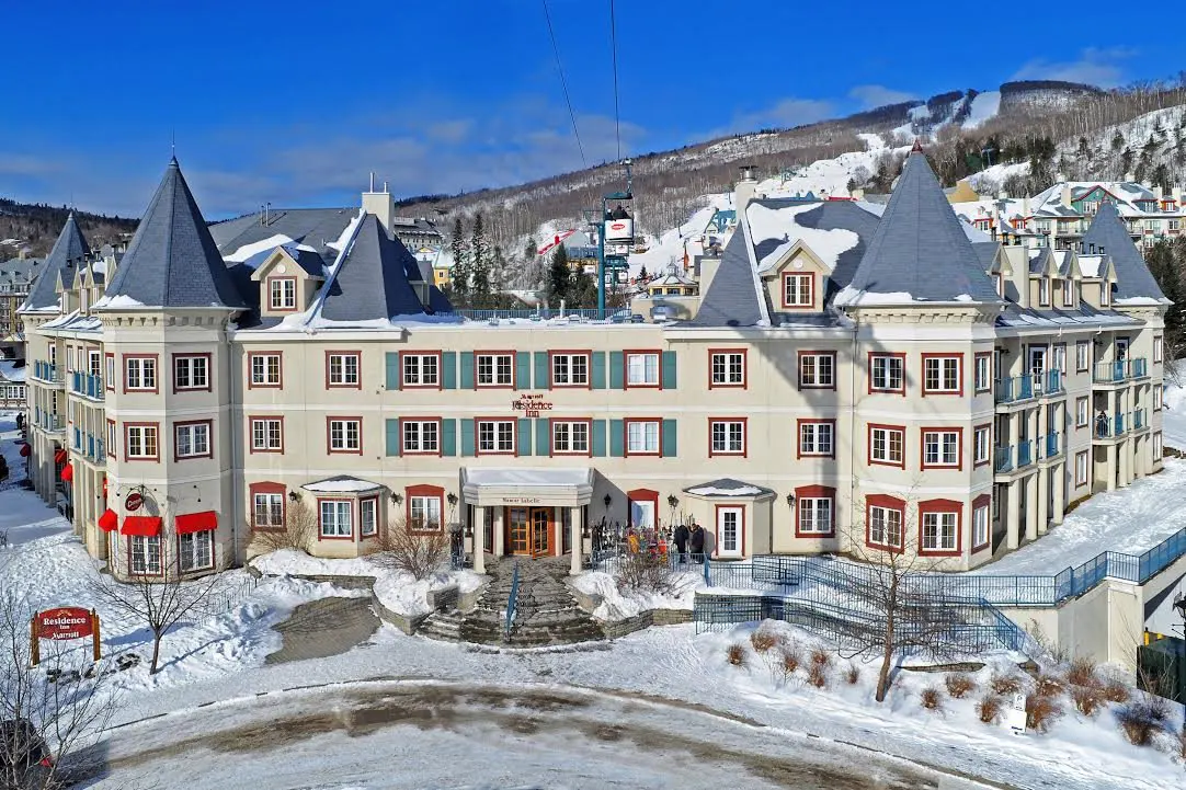 Hotel Residence Inn in winter. Beige building with blue shutters and roof. Ski lift in background.