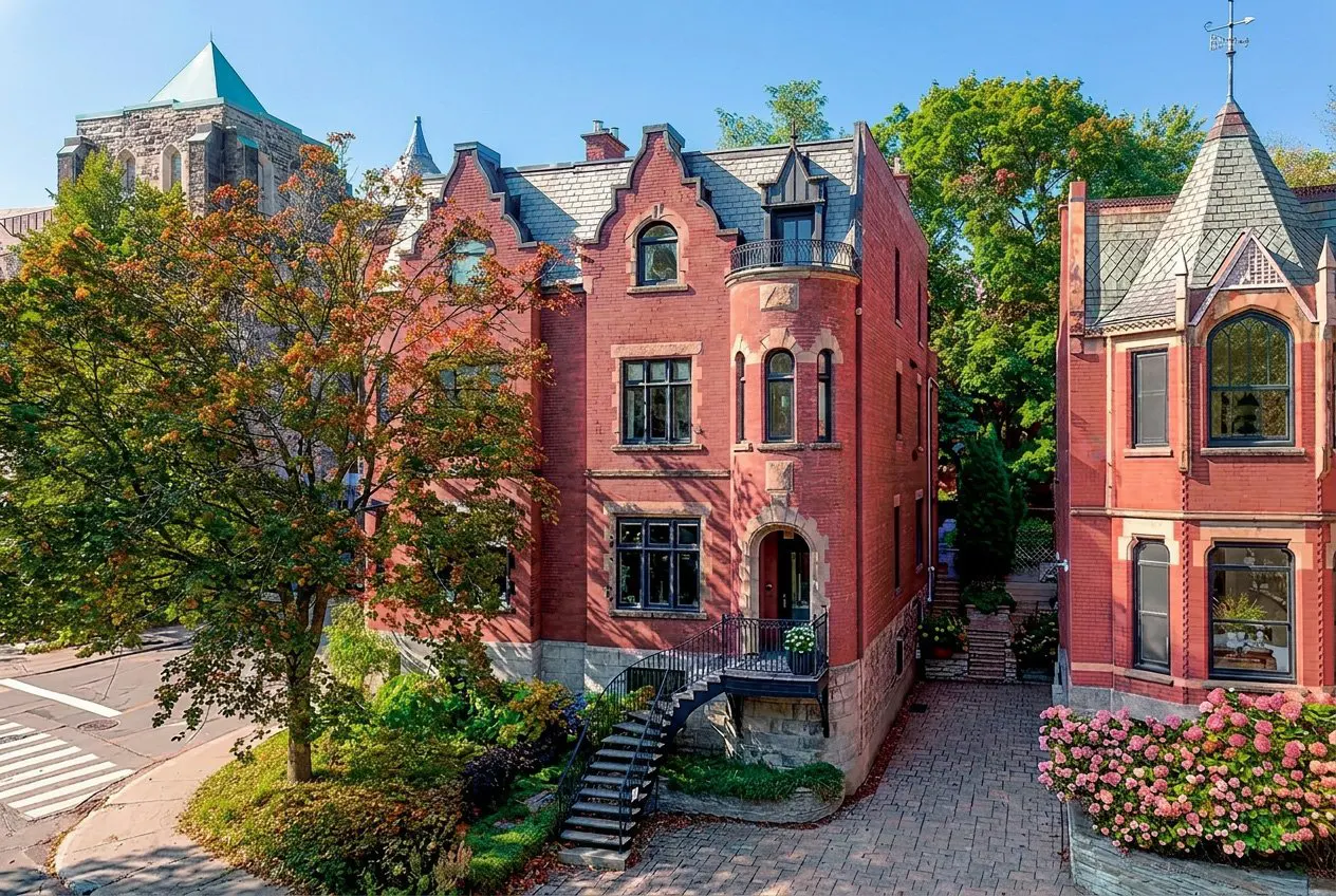 Exterior view of a red brick Victorian house with black framed windows and a slate roof on a sunny day.