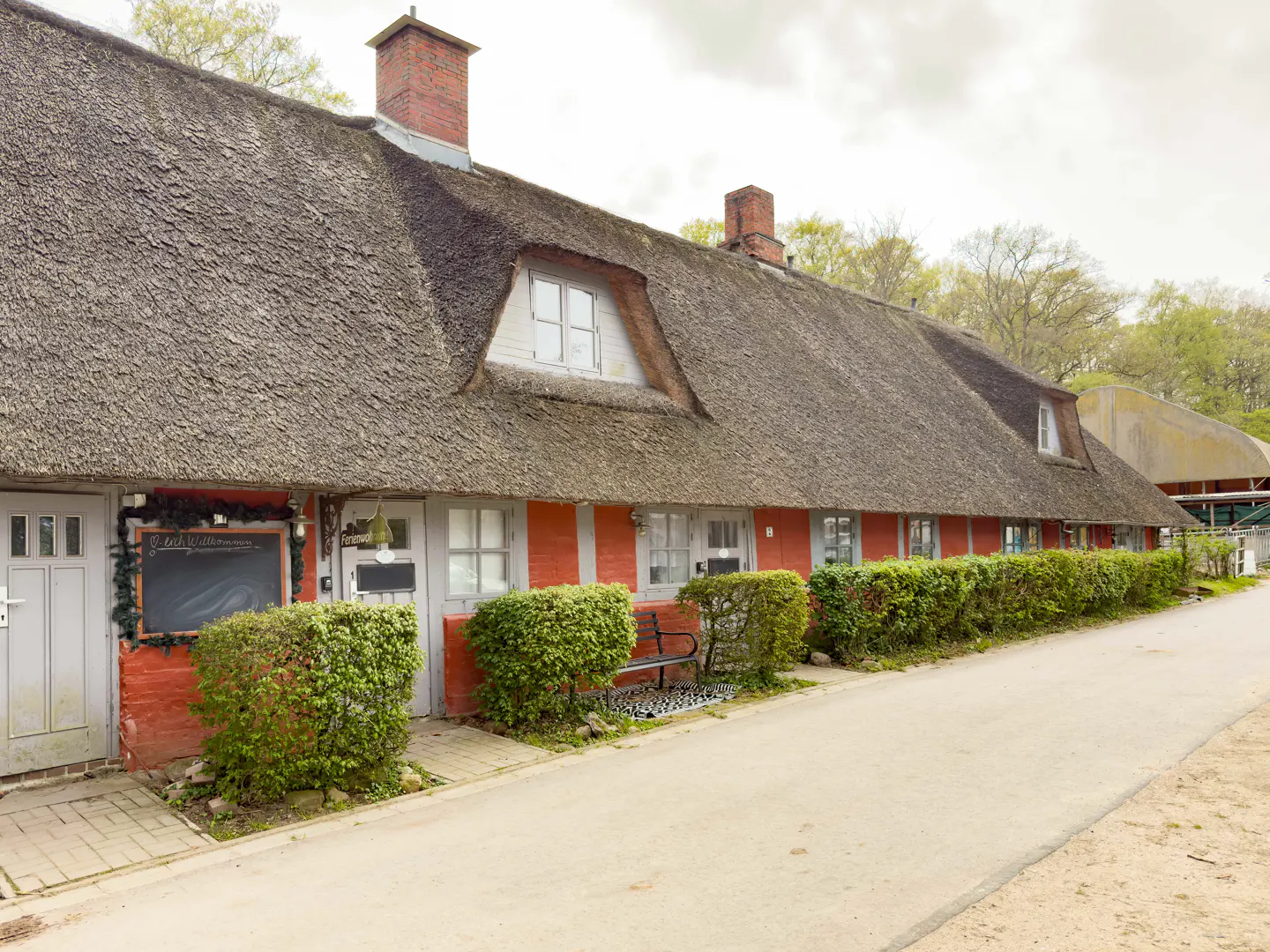Exterior of a red building with a thatched roof, trimmed hedges, and a gray door.