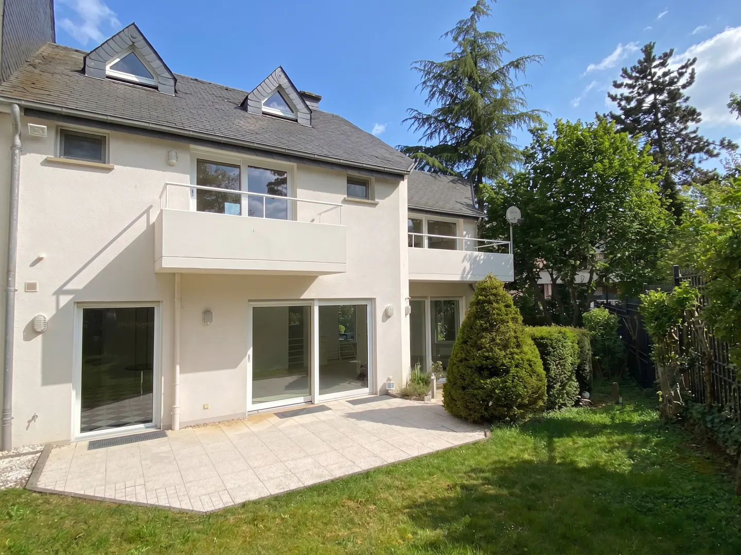 Back of a two-story white house with balconies, sliding glass doors, and a stone patio leading to a green lawn.