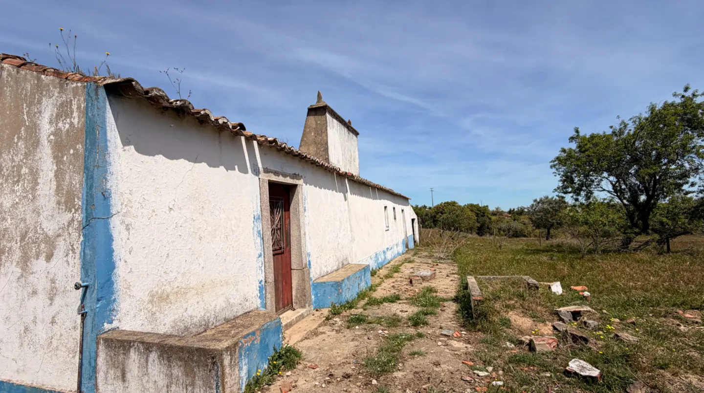 Exterior view of a white, one-story building with a red door and blue trim, set against a blue sky and grassy landscape.