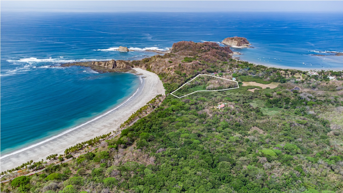 Aerial view of a beachside property outlined in white, bordered by lush green forest and the blue ocean.
