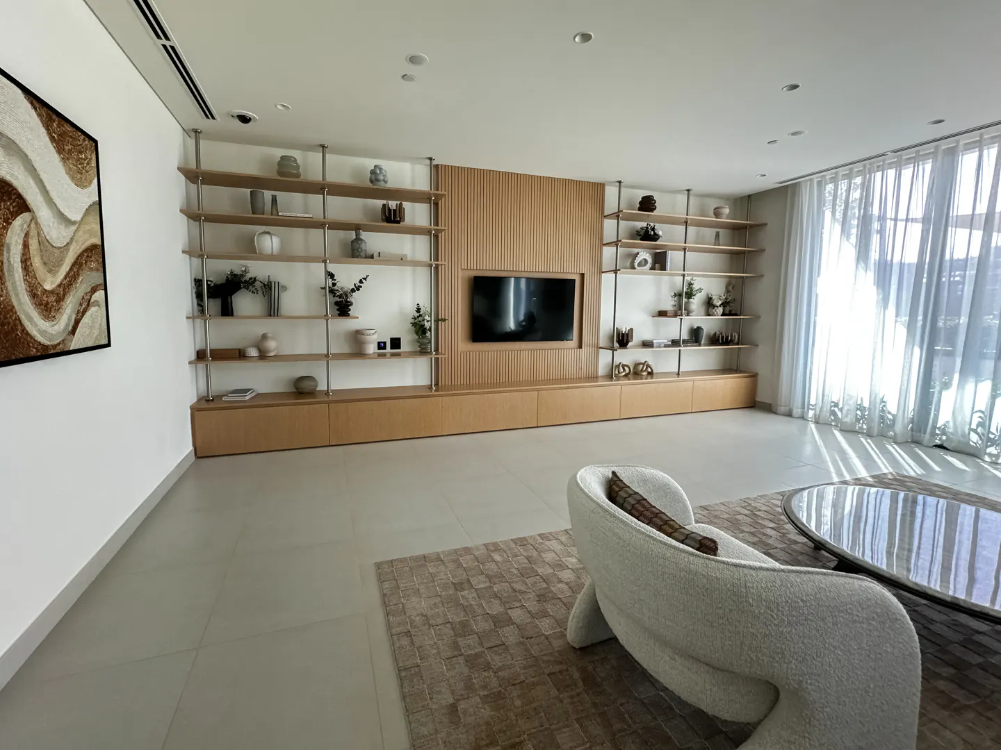 Bright living room with a white chair, a brown rug, and a long wooden shelf with a TV in the middle.