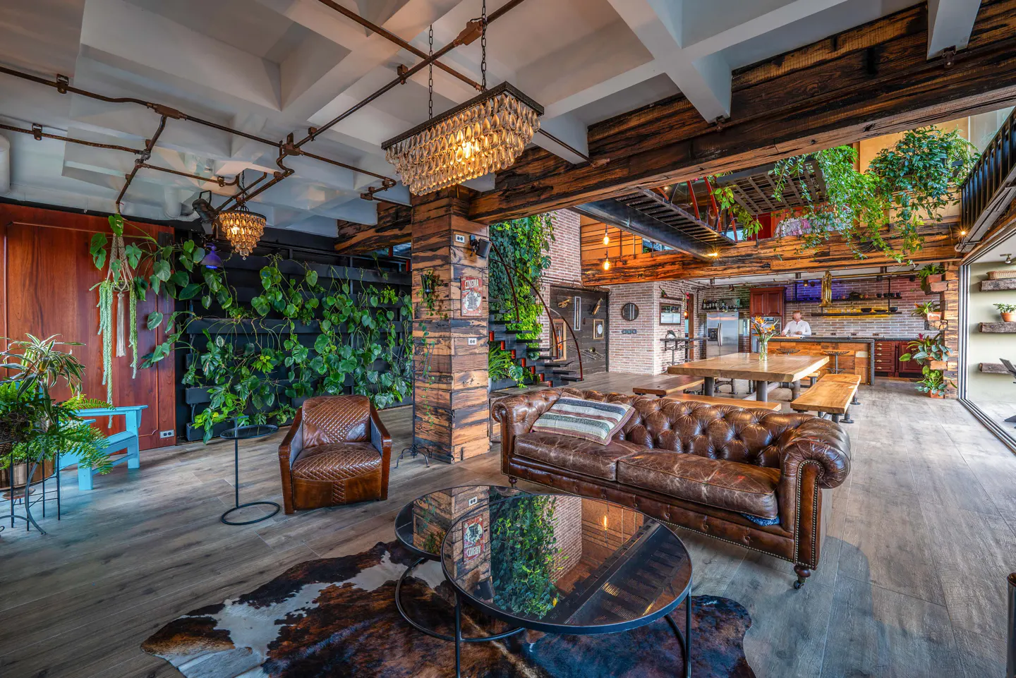 Living room with a brown leather sofa, chair, and cowhide rug. A green wall and wooden beams add natural elements.
