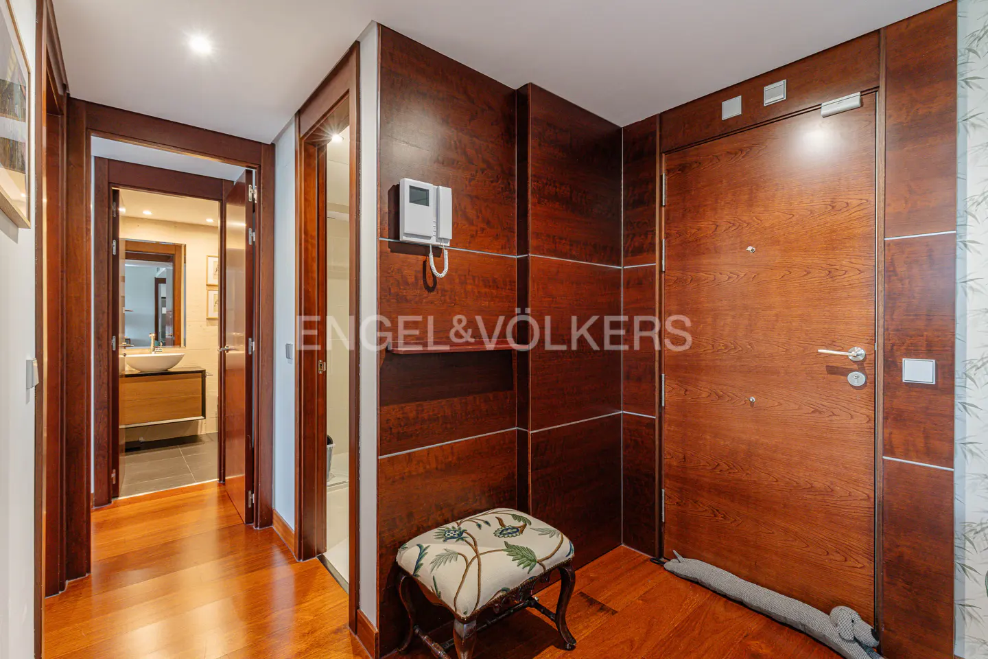 A foyer with wood floors, a wood paneled wall with an Engel & Völkers logo, and a door.