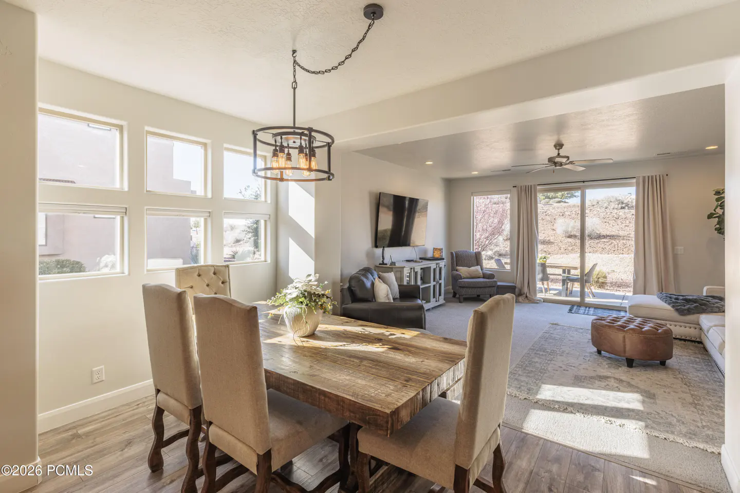 Dining area with a rustic wood table and beige chairs, opening into a living room with a TV, sofa, and patio access.