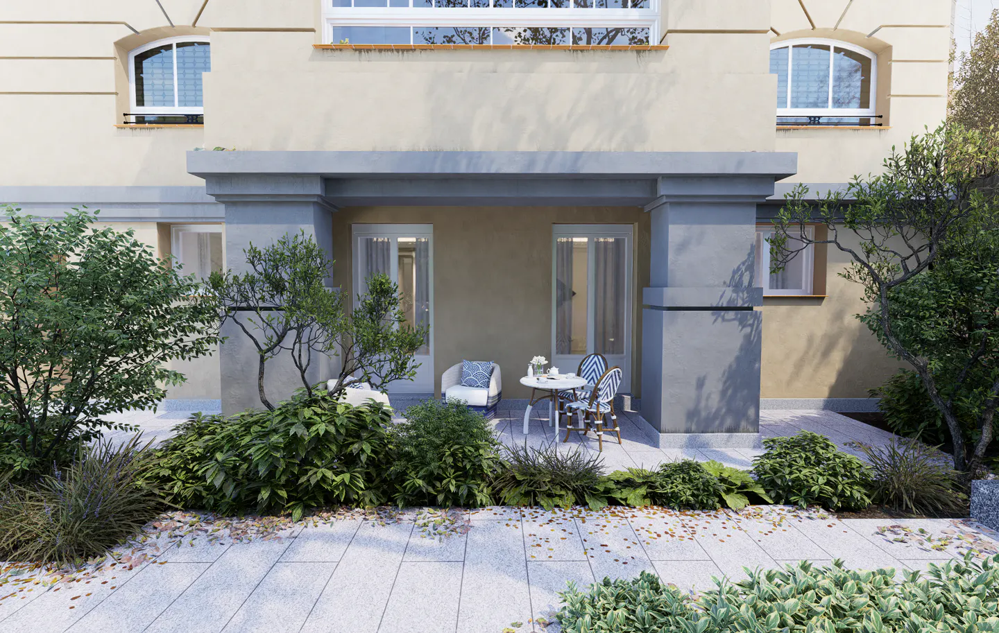 A beige building exterior with a covered patio featuring a small bistro table, two chairs, and lush garden landscaping.