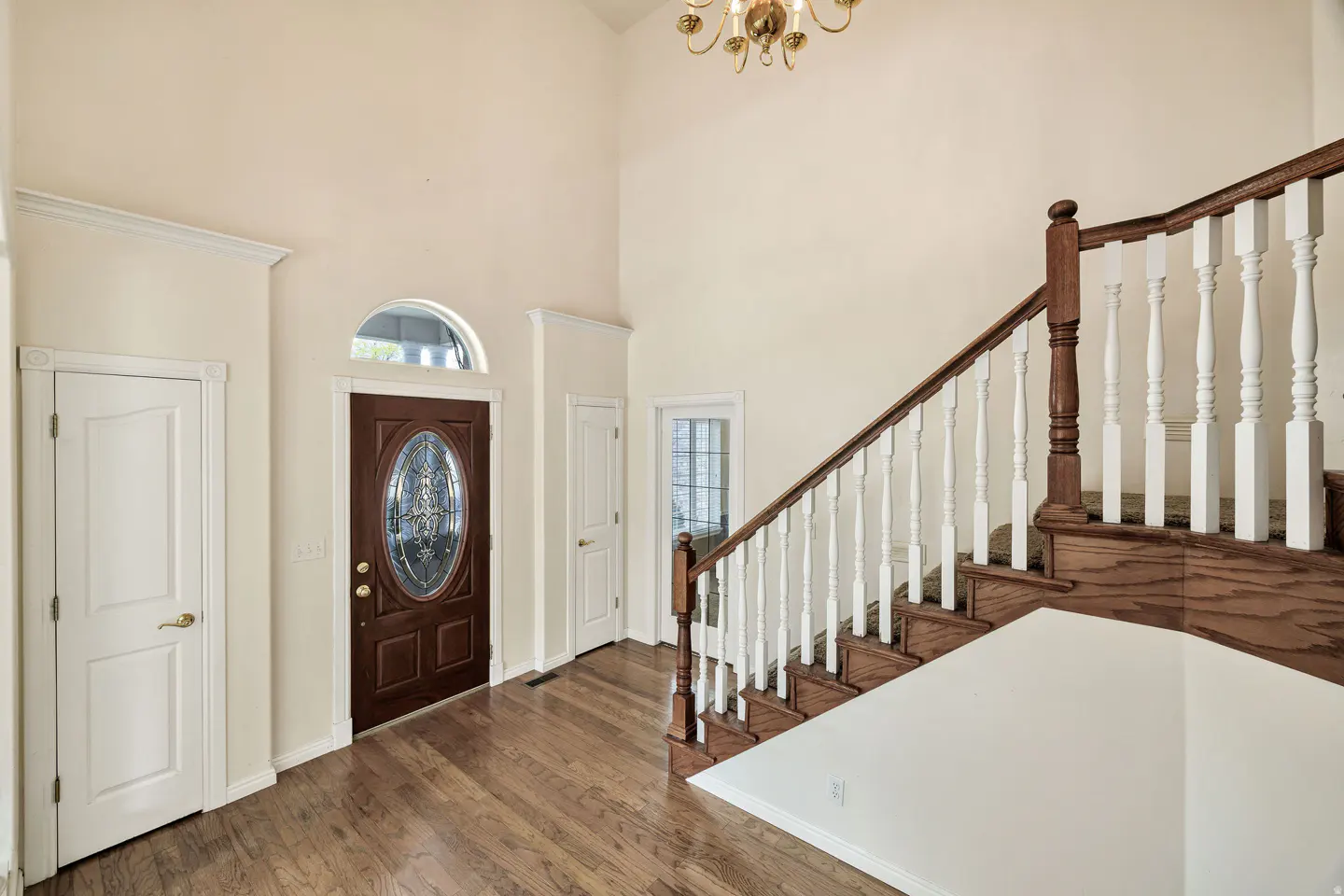 Foyer with hardwood floors, a brown front door with an oval window, and a staircase with white balusters and a wood banister.