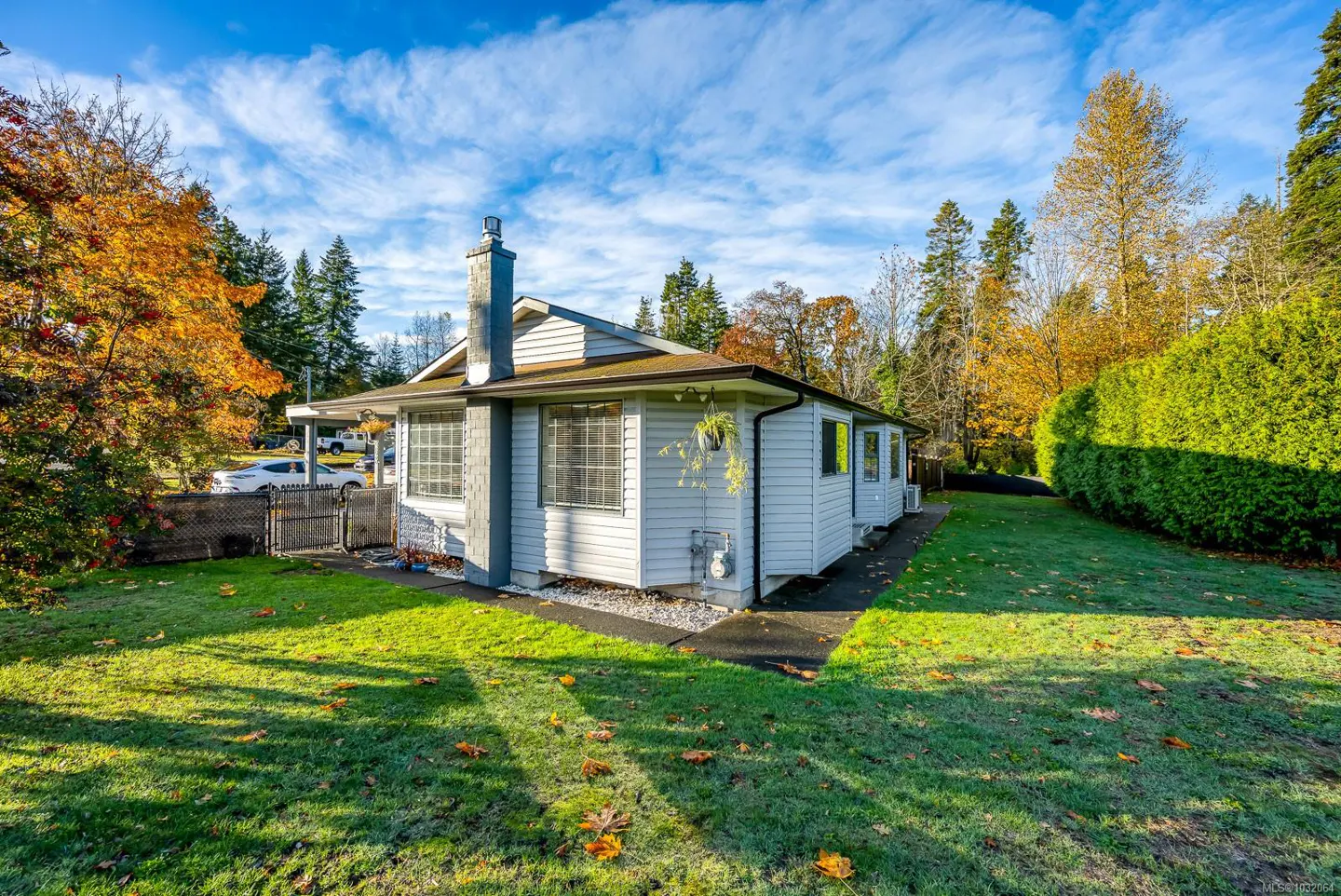 A white, one-story house with a chimney, surrounded by green lawn and trees with autumn foliage under a blue sky.