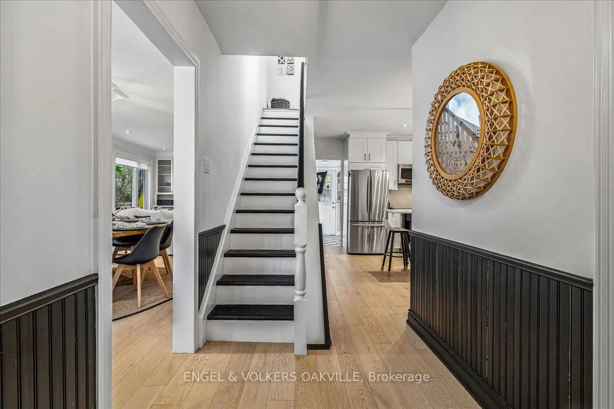 Interior view of a home's entryway with black and white stairs, a round mirror, and glimpses of the dining room and kitchen.