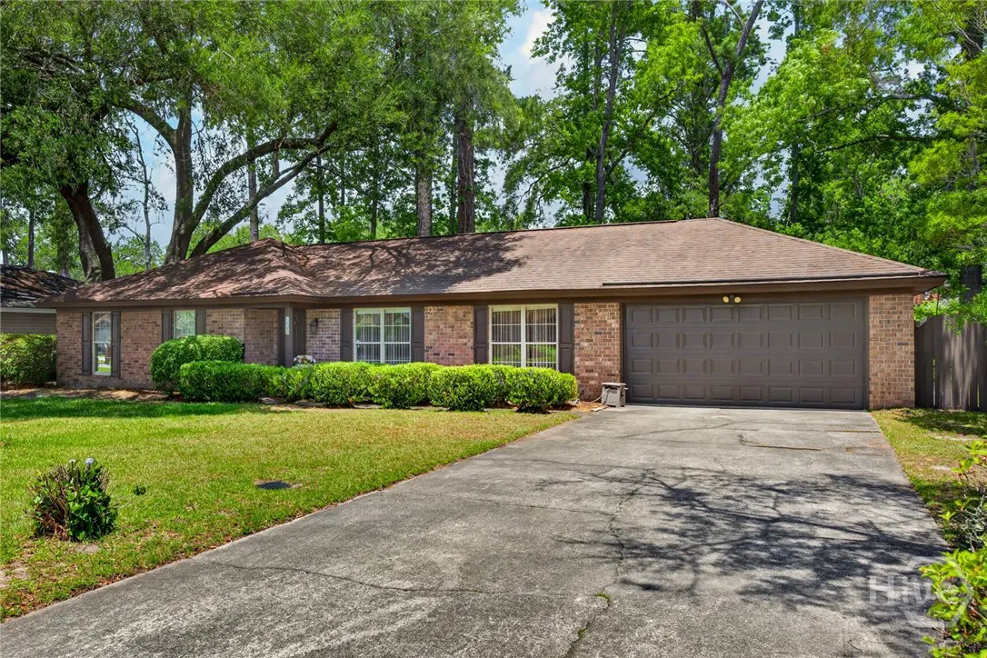 A single-story brick house with a brown roof, a gray garage door, and a green lawn.