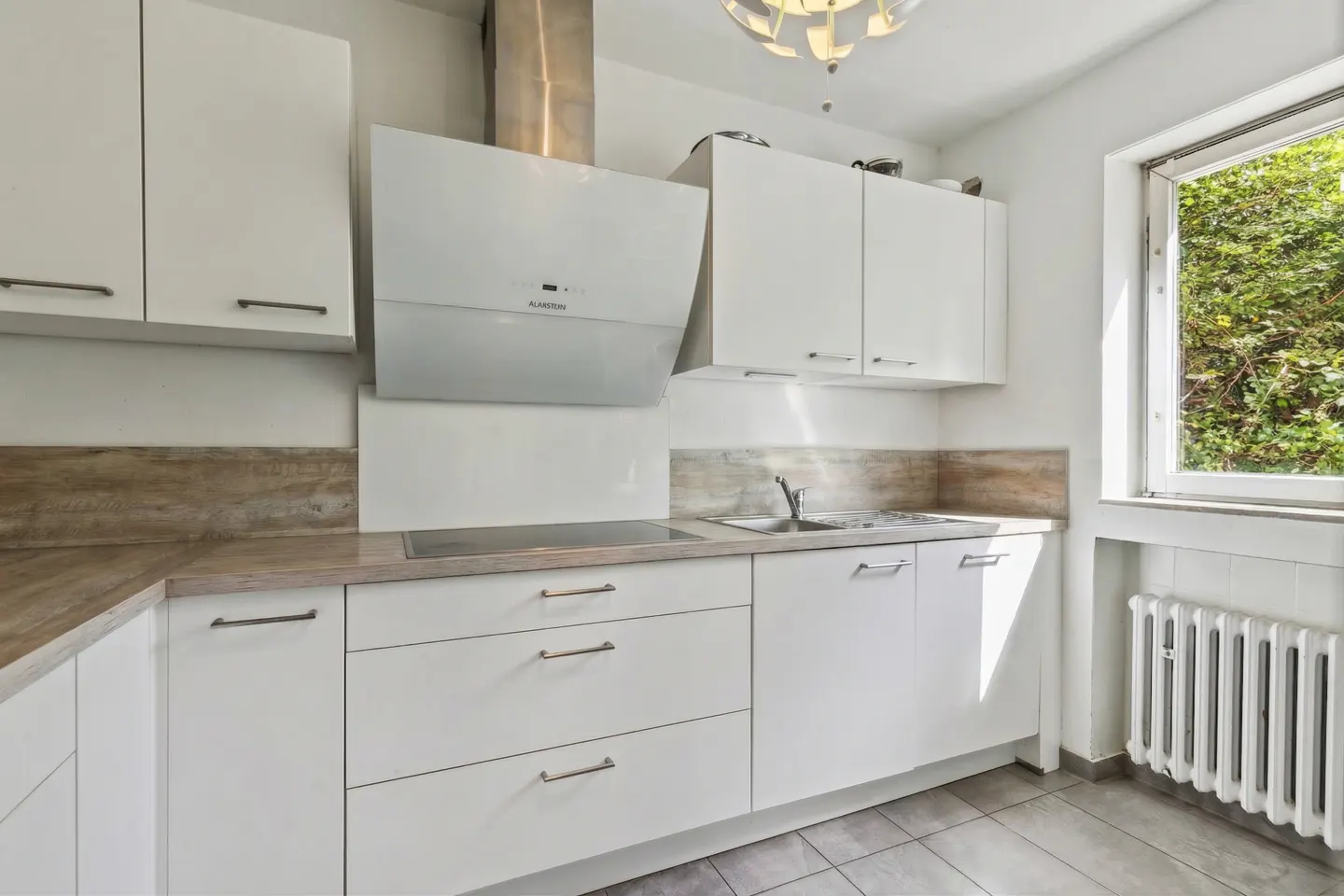 Bright kitchen with white cabinets, stainless steel hood, and wood-look countertops. A window shows green foliage outside.