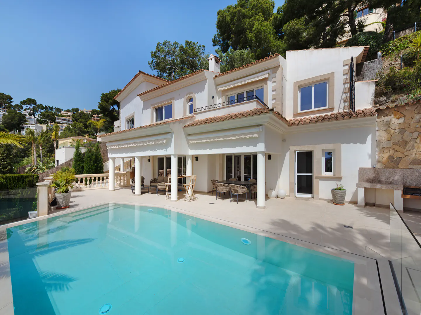 Exterior of a white, two-story house with a red tile roof and a blue swimming pool in the foreground.