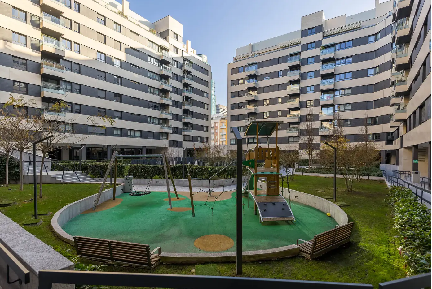 Apartment complex with a playground. The playground has swings, a slide, and benches. The buildings are modern with black and white stripes.