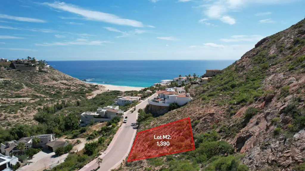 Aerial view of Lot M2, 1,390, outlined in red, on a hillside near a road, with ocean and houses in the background.